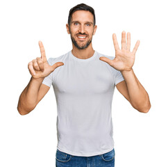 Handsome man with beard wearing casual white t shirt showing and pointing up with fingers number seven while smiling confident and happy.