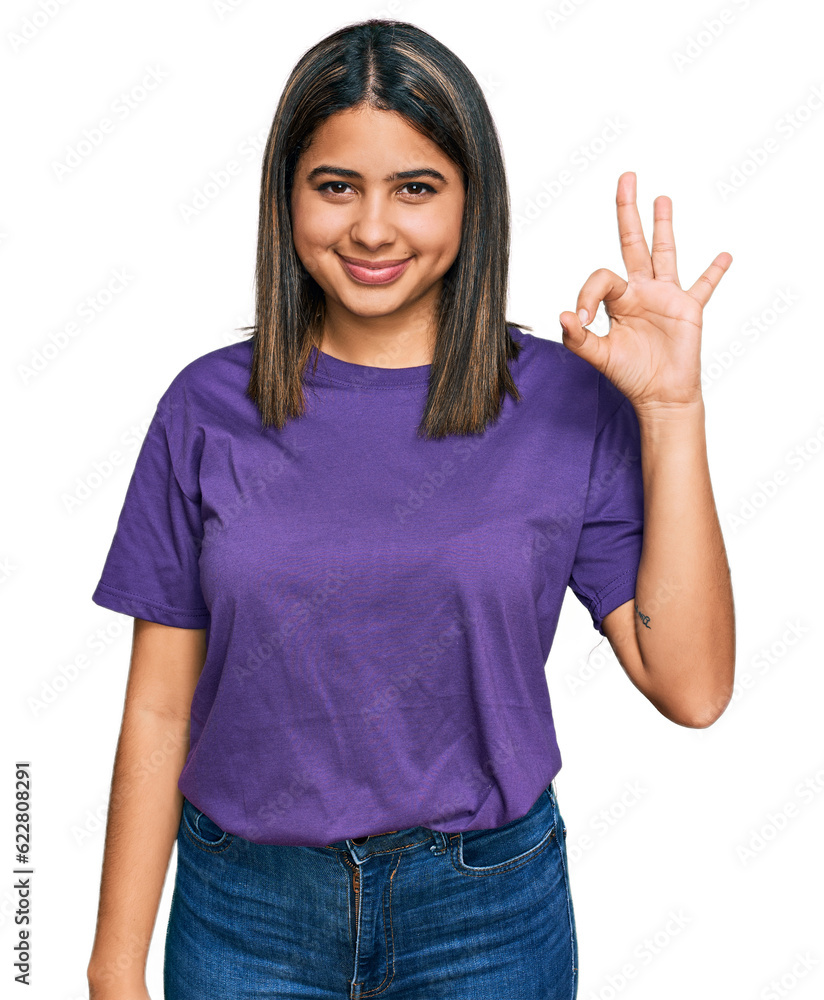 Wall mural Young hispanic girl wearing casual purple t shirt smiling positive doing ok sign with hand and fingers. successful expression.