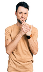 Hispanic man with beard wearing casual t shirt suffering pain on hands and fingers, arthritis...