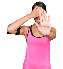 Beautiful asian young sport woman wearing sportswear and arm band covering eyes with hands and...