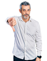 Middle age hispanic with grey hair wearing casual white shirt looking unhappy and angry showing rejection and negative with thumbs down gesture. bad expression.