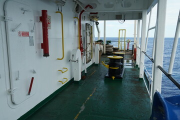 Entrance to white superstructure of container merchant vessel from  main deck painted green on port side. There are black bollard, red fire plan tube and mooring ropes in aft manoeuvring station.