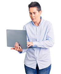 Young woman with short hair holding laptop thinking attitude and sober expression looking self confident