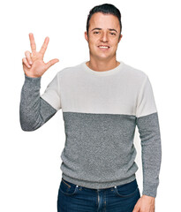 Fototapeta premium Handsome young man wearing casual winter sweater showing and pointing up with fingers number three while smiling confident and happy.