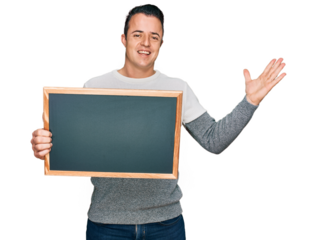 Handsome young man holding blackboard celebrating victory with happy smile and winner expression with raised hands