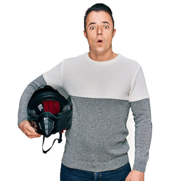 Handsome young man holding motorcycle helmet scared and amazed with open mouth for surprise, disbelief face
