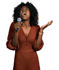 African woman with curly hair singing song using microphone crazy and mad shouting and yelling with...