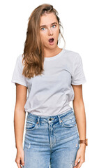 Fototapeta premium Beautiful young blonde woman wearing casual white t shirt in shock face, looking skeptical and sarcastic, surprised with open mouth