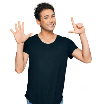 Young handsome man wearing casual black t shirt showing and pointing up with fingers number seven while smiling confident and happy.