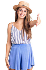 Young beautiful blonde woman wearing summer hat smiling friendly offering handshake as greeting and welcoming. successful business.
