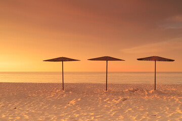 Słomiane, plażowe parasole na plaży w Helu o wschodzie słońca.