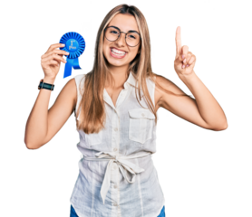 Hispanic young woman holding first place badge smiling with an idea or question pointing finger with happy face, number one