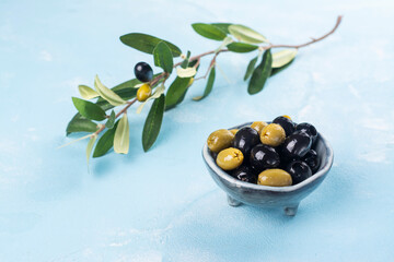 Black and green greek olives in a bowl on blue sunny background. Copy space