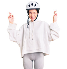 Beautiful brunette young woman wearing bike helmet and sporty clothes gesturing finger crossed smiling with hope and eyes closed. luck and superstitious concept.