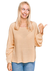 Young blonde girl wearing casual clothes smiling with happy face looking and pointing to the side with thumb up.