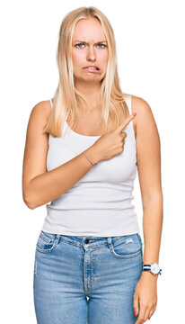 Young blonde girl wearing casual style with sleeveless shirt pointing aside worried and nervous with forefinger, concerned and surprised expression