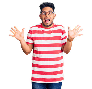 Handsome latin american young man wearing casual clothes and glasses celebrating crazy and amazed for success with arms raised and open eyes screaming excited. winner concept