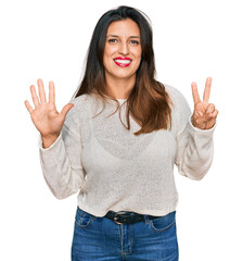 Beautiful hispanic woman wearing casual sweater showing and pointing up with fingers number seven while smiling confident and happy.