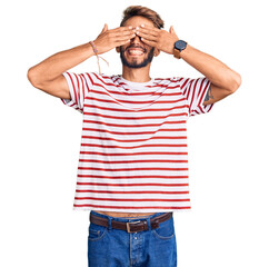 Fototapeta premium Handsome blond man with beard wearing casual clothes and glasses covering eyes with hands smiling cheerful and funny. blind concept.