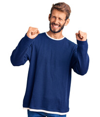 Handsome blond man with beard wearing casual sweater angry and mad raising fists frustrated and furious while shouting with anger. rage and aggressive concept.