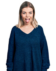 Young blonde woman wearing casual sweater sticking tongue out happy with funny expression. emotion concept.