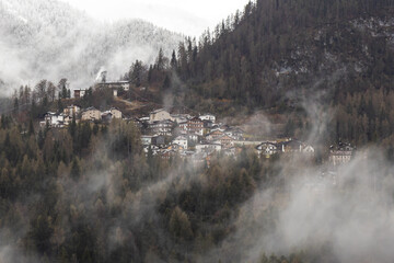 View of Cibiana di Cadore, small town in the mountains in a misty winter day; Snow peaked mountains on the background; Belluno, Italy; Dolomites