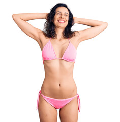 Obraz premium Young beautiful hispanic woman wearing bikini relaxing and stretching, arms and hands behind head and neck smiling happy