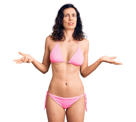 Fototapeta premium Young beautiful hispanic woman wearing bikini clueless and confused with open arms, no idea concept.