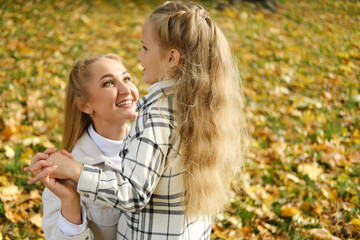 Fototapeta premium Mother and daughter spend time together in the autumn park. Mother looks at her daughter and smiles