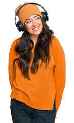 Beautiful brunette young woman listening to music using headphones looking away to side with smile on face, natural expression. laughing confident.