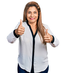 Middle age latin woman wearing business shirt approving doing positive gesture with hand, thumbs up smiling and happy for success. winner gesture.