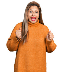 Middle age latin woman wearing turtleneck sweater celebrating surprised and amazed for success with arms raised and open eyes. winner concept.