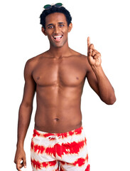 African handsome man wearing swimsuit and sunglasses showing and pointing up with finger number one while smiling confident and happy.