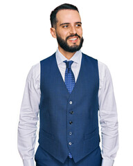 Young man with beard wearing business vest looking away to side with smile on face, natural expression. laughing confident.