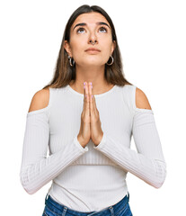 Young hispanic woman wearing casual clothes begging and praying with hands together with hope...
