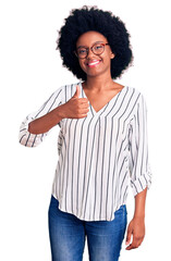 Young african american woman wearing casual clothes and glasses doing happy thumbs up gesture with hand. approving expression looking at the camera showing success.