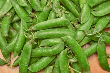 green ripe plucked pea pods on a wooden kitchen cutting board close-up. flat lay