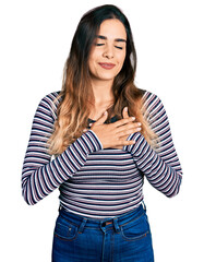 Beautiful hispanic woman wearing casual striped shirt smiling with hands on chest with closed eyes and grateful gesture on face. health concept.