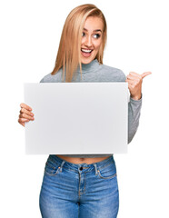 Fototapeta premium Beautiful caucasian woman holding blank empty banner pointing thumb up to the side smiling happy with open mouth