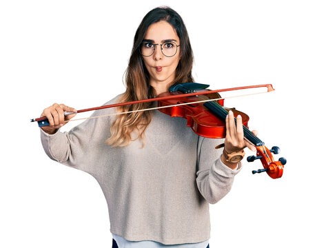 Beautiful hispanic woman playing violin making fish face with mouth and squinting eyes, crazy and comical.