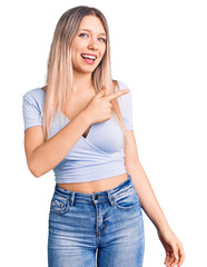 Young beautiful blonde woman wearing casual clothes cheerful with a smile of face pointing with hand and finger up to the side with happy and natural expression on face