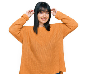 Young hispanic woman wearing casual clothes smiling pulling ears with fingers, funny gesture....