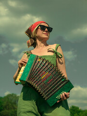 blonde with a short haircut with an accordion in sunglasses in a green jumpsuit in nature 