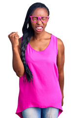 Obraz na płótnie Canvas Young african american woman wearing casual clothes and glasses angry and mad raising fist frustrated and furious while shouting with anger. rage and aggressive concept.