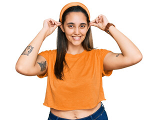 Young hispanic woman wearing casual clothes smiling pulling ears with fingers, funny gesture....