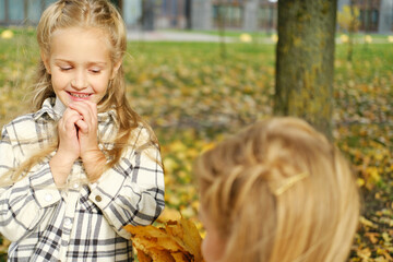The family spends time together in the autumn park. Daughter gives her mother a bouquet of autumn leaves