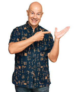 Middle age bald man wearing casual clothes amazed and smiling to the camera while presenting with hand and pointing with finger.