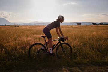 Fit female cyclist wearing cycling kit and helmet riding on the road on a gravel bike at...