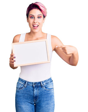 Young beautiful woman with pink hair holding empty white chalkboard smiling happy pointing with hand and finger