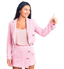 Young beautiful latin girl wearing business clothes looking proud, smiling doing thumbs up gesture to the side